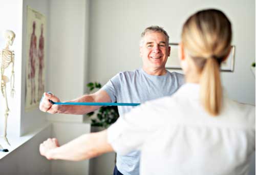 Naples physiotherapy specialist helping mature man with arm exercise