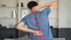 Man Suffering from Backache at Home, Spinal Disc Disease, Painful Area Highlighted in Red