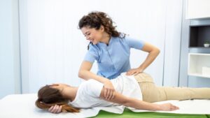 Young Woman Chiropractor Fixing Lying Woman's Back with Hand Movements